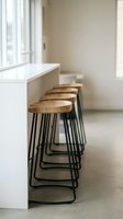 Row of wooden bar stools with black metal legs positioned at white counter in modern minimalist interior space with natural light from window.
