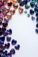 Colorful heart-shaped crystal gems arranged in rainbow gradient from pink to blue on white background, creating romantic border design for valentines and love themes.