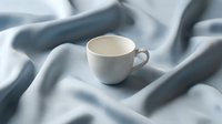 White ceramic cup on soft blue and gray fabric, ideal for beverage, home decor, and lifestyle design projects.