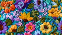 Vibrant embroidered floral pattern with colorful blooms in orange, purple, pink and turquoise on blue fabric background, featuring detailed stitching and textural elements.