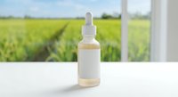 Natural skincare serum bottle with dropper on white surface against green field background for organic cosmetic product marketing and wellness branding.