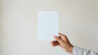 Caucasian male hand holding blank white paper sheet against neutral beige background, suitable for mockups, presentations, and advertising campaigns.