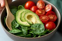 Fresh avocado and cherry tomato salad bowl with spinach leaves and wooden spoon for healthy eating and nutrition concepts.