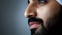 Close up profile portrait of Middle Eastern man with well-groomed beard and intense blue eyes against dark background, dramatic side lighting creates mood.