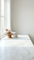 Minimalist kitchen counter with marble surface, wooden pedestal bowl containing fresh oranges, natural window light creating serene modern interior atmosphere.