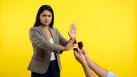 Young Hispanic businesswoman in beige blazer making stop gesture refusing alcohol bottles on bright yellow background for addiction awareness campaigns.