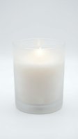 White candle burning in a frosted glass jar on a light background, evoking calm and relaxation for spa, wellness, and home decor concepts.