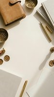 Flat lay workspace with tan leather wallet, gold pens, notebooks, and brass desk accessories arranged on white background for business and office design projects.