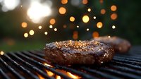 Juicy steak grilling on barbecue with bokeh lights in background. Meat seared to perfection showing grill marks and seasonings on outdoor cooking grate.