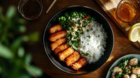 Crispy breaded chicken cutlets served with steamed white rice and fresh chopped herbs in black bowl on wooden table, top view. Asian fusion cuisine.