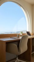 Modern workspace with wooden desk and upholstered chair positioned at large circular window overlooking mountain landscape. Natural light floods minimalist office interior, ideal for remote work and productivity concepts.