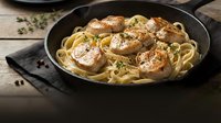Pan-seared scallops with creamy pasta in cast iron skillet, garnished with fresh herbs and black pepper for gourmet seafood dining experience.