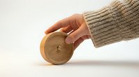 Hand in cozy knit sweater holding a round wooden object on white background, minimalist eco-friendly design concept.