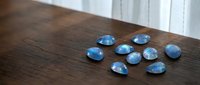 Blue gemstones scattered on wooden surface with natural lighting creating elegant jewelry display for luxury accessories and precious stone collection.