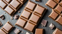 Broken milk chocolate bars and pieces scattered on dark stone background, creating appetizing composition with rich texture and warm brown tones for food photography.
