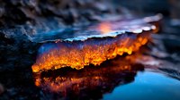 Dramatic contrast of glowing orange lava flow against dark volcanic rock, with vibrant blue sky reflection creating a mesmerizing natural phenomenon scene.