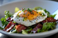 Fresh salad with crispy bacon strips and sunny side up egg on top, garnished with herbs and black pepper, served on white plate for breakfast or brunch.