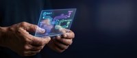 Male hands holding transparent digital tablet displaying holographic interface with data visualization and circuit patterns against dark background.