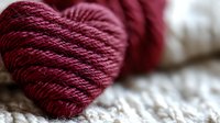 Burgundy yarn ball on soft white knitted fabric, showcasing rich texture and warm color contrast for crafting and knitting projects.