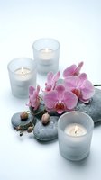 Spa wellness setup with pink orchid flowers, lit candles in frosted glass holders and smooth stones for relaxation and meditation therapy.