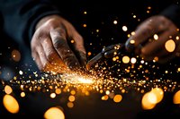 Close up of African American hands working with metal creating bright orange sparks and bokeh light effects against dark background. Industrial craftsmanship.