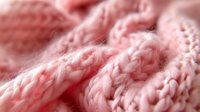 Pink knitted wool texture in macro view showing soft yarn details and intricate stitch pattern, creating cozy winter background for design projects.