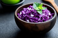 Fresh shredded purple cabbage in wooden bowl garnished with mint leaf on dark background, healthy vegetarian food for salads and coleslaw.