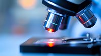 Close-up view of microscope lens with red laser light illuminating glass slide against blurred blue laboratory background, scientific research concept.