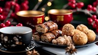 Festive winter dessert setting with fresh pastries, coffee cups, walnuts and red berries against blurred holiday lights background, cozy seasonal atmosphere.