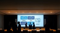 Silhouettes of diverse professionals standing before large projection screen displaying digital icons and workflow diagrams during corporate presentation or business training seminar.