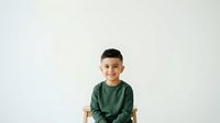 Young boy with dark hair and olive complexion wearing a green long-sleeve shirt, smiling at camera against white background. Suitable for family, education, and lifestyle design projects.