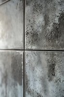 Close-up view of modern metallic tiles with textured surface showing industrial wear pattern and oxidized finish. Architectural detail for contemporary interior design.