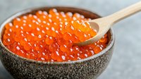 Red salmon caviar in ceramic bowl with wooden spoon on gray background, fresh luxury seafood delicacy close up view for gourmet restaurant menu.
