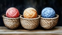 Three woven baskets containing yarn balls in pink, beige and blue colors arranged in row on wooden surface against dark background. Crafting and knitting concept.