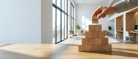 Hand placing a wooden block labeled Trust on top of a pyramid structure in a bright modern office, symbolizing business integrity.