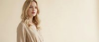 Young blonde Caucasian woman in beige minimalist outfit against neutral background for fashion and lifestyle content.
