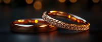 Elegant wedding rings with diamonds on dark background with golden bokeh lights, one plain band and one eternity ring showing luxury and romance.