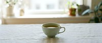Green ceramic cup filled with tea on marble countertop near window with plants, suitable for beverage, lifestyle, and home decor designs.
