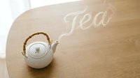 White ceramic teapot with bamboo handle on wooden table, steam forming the word Tea, cozy home atmosphere, top view.