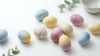 Colorful pastel Easter eggs in soft blue, pink and yellow tones scattered on white surface with eucalyptus leaves for spring holiday celebration.