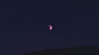 Pink glowing moon rising over dark mountain silhouette against deep purple night sky, creating mystical atmospheric landscape for nature and astronomy designs.