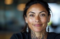 Professional Hispanic woman with traditional tattoos smiling confidently in modern office environment for business and career success concepts.