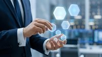 Businessman in formal suit holding glowing hexagonal digital icons with blurred city skyline background, representing technology, innovation, and business solutions.