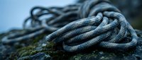 Coiled climbing rope on rocky surface with moss, outdoor adventure equipment for mountaineering and rock climbing activities in natural mountain environment.
