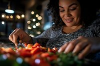Woman with medium skin tone and curly dark hair, wearing a gray sweater, preparing fresh vegetables in warm holiday lighting for cooking or meal preparation.