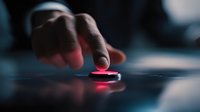 Young man pressing glowing red button with finger on dark surface creating dramatic lighting effect for technology and decision-making concepts.