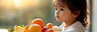 Young Asian toddler girl enjoying fresh oranges and healthy fruits during sunny breakfast time, promoting nutritious eating habits for children.