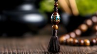 Decorative oriental tassel pendant with metallic bead and wooden prayer beads on dark wooden surface, selective focus on ornate details in soft natural lighting.