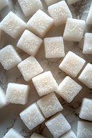 White sugar cubes scattered on rustic wooden surface with granulated texture for cooking and baking concepts.
