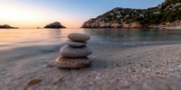 Zen stone stack on peaceful beach at sunset with calm waters and rocky coastline creating serene meditation atmosphere for wellness and mindfulness practices.